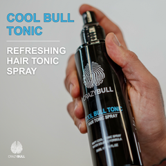 Hand holding a bottle of Crazy Bull Cool Bull Tonic refreshing hair tonic spray against a plain background.